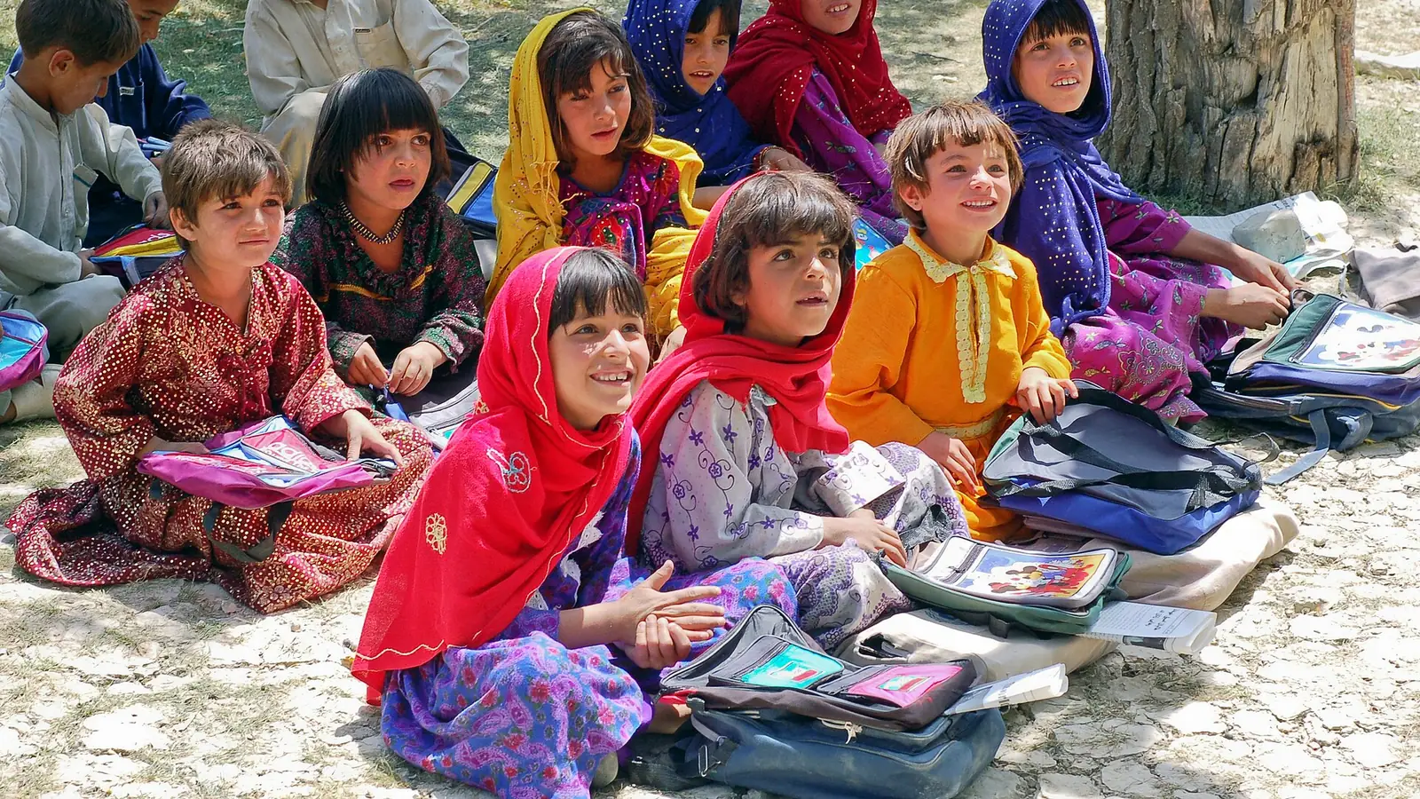Afghan schoolgirls in colourful headscarves sitting outdoors with their books