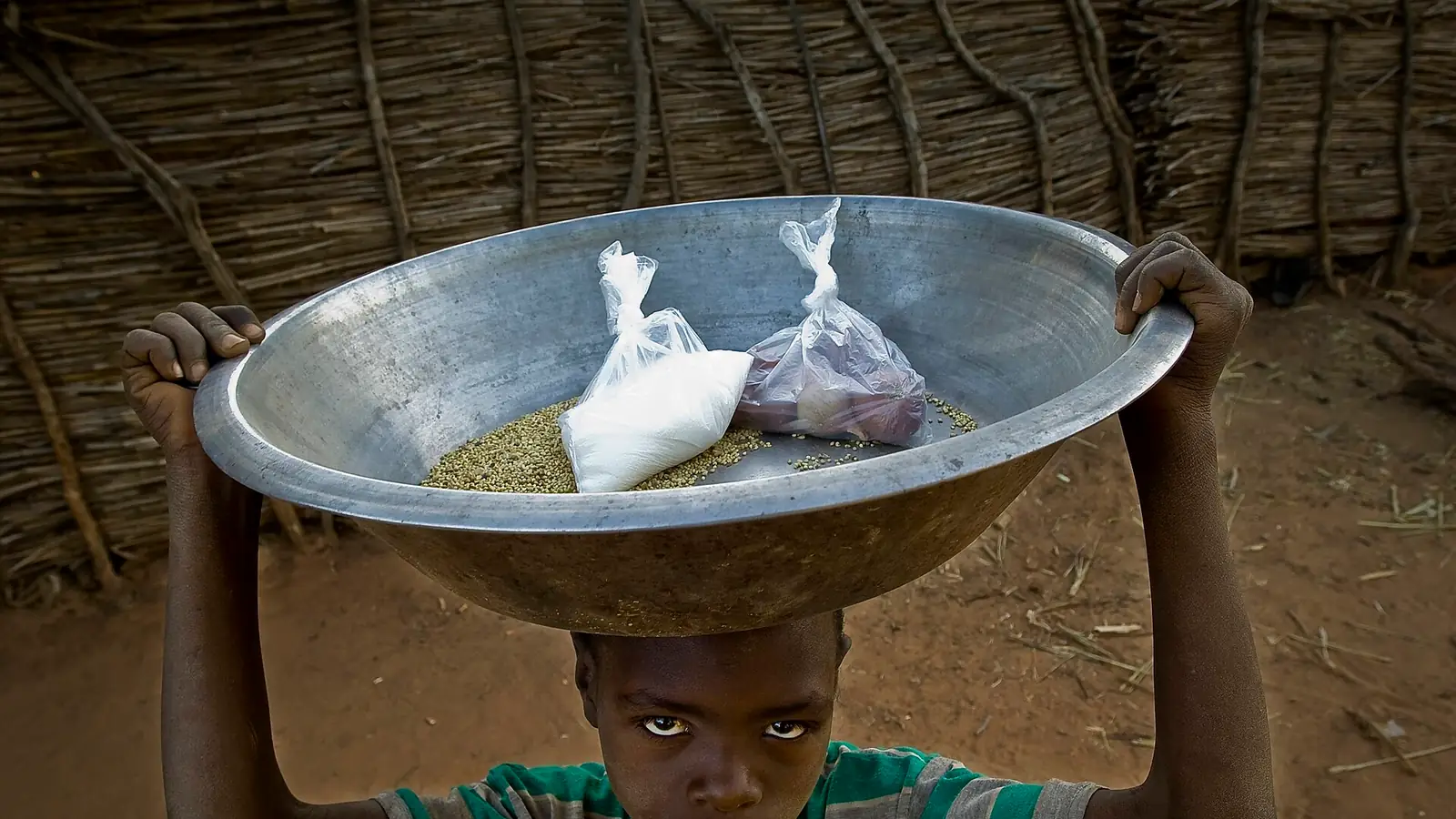 A Darfuri refugee girl carrying a metal bowl of food on her head